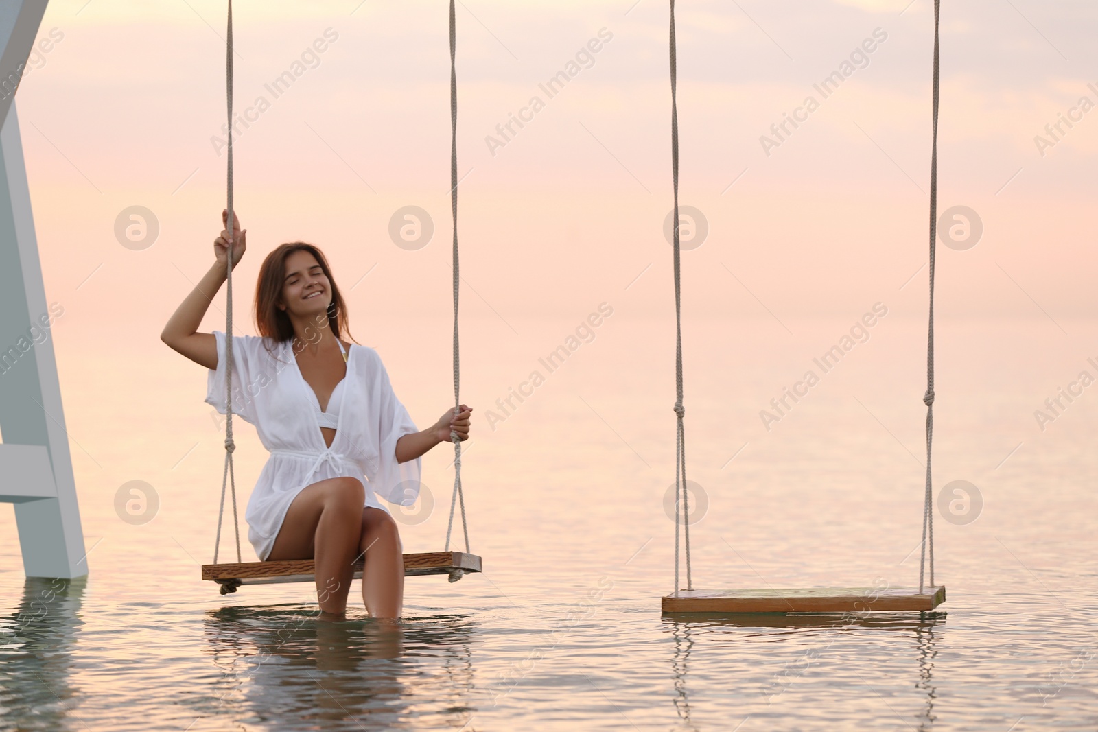 Young woman enjoying sunrise on swing over water Photo of Young woman enjoying sunrise on swing over water
