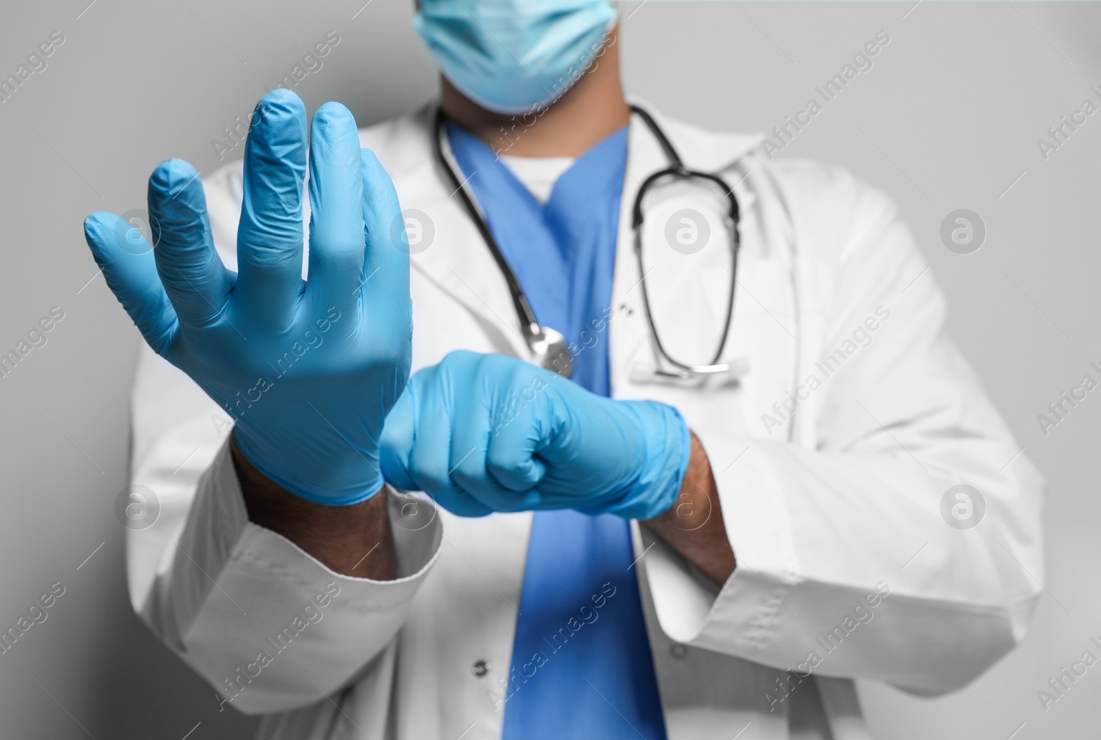 Doctor in protective mask putting on medical gloves against light grey background, closeup Photo of Doctor in protective mask putting on medical gloves against light grey background, closeup