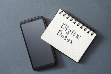 Notebook with phrase DIGITAL DETOX and smartphone on grey background, flat lay Photo of Notebook with phrase DIGITAL DETOX and smartphone on grey background, flat lay