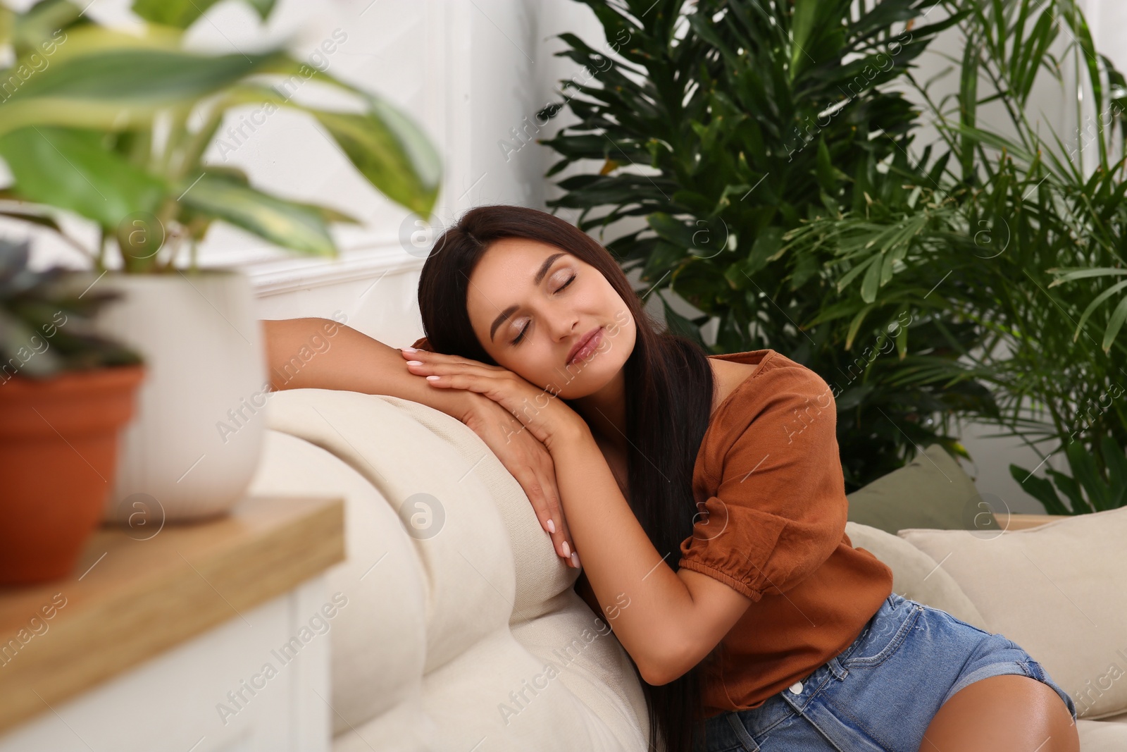 Beautiful woman sitting on sofa in living room decorated with houseplants. Interior design Photo of Beautiful woman sitting on sofa in living room decorated with houseplants. Interior design