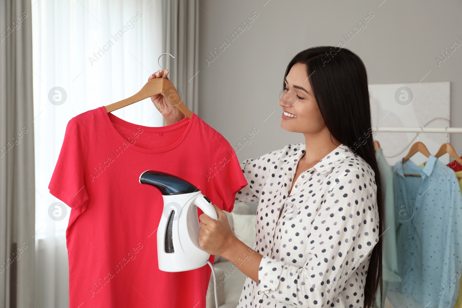 Woman steaming t-shirt on hanger at home Photo of Woman steaming t-shirt on hanger at home