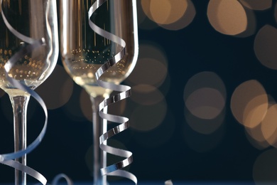 Glasses of champagne and serpentine streamers against dark blue background with blurred lights, closeup. Space for text Photo of Glasses of champagne and serpentine streamers against dark blue background with blurred lights, closeup. Space for text