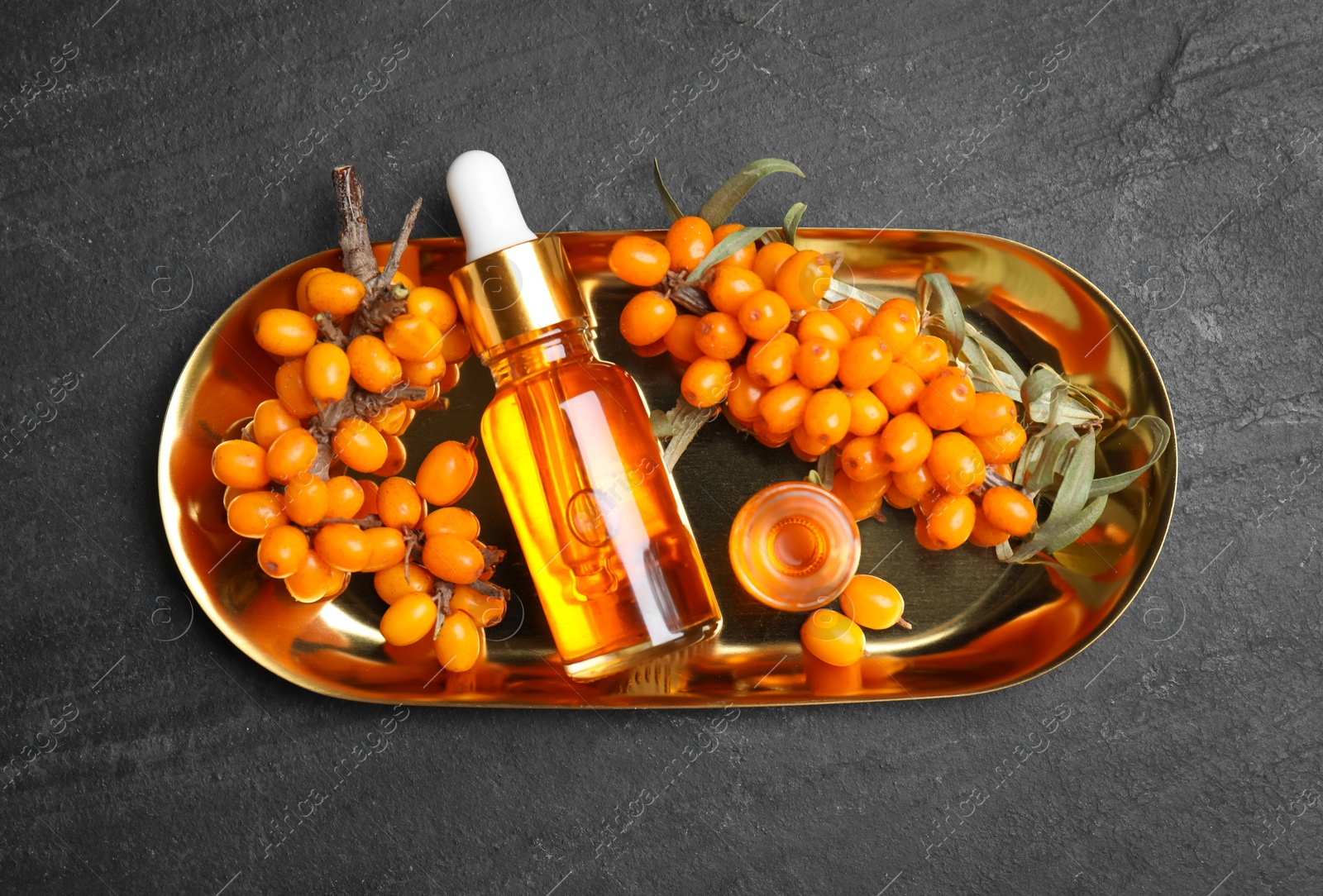 Ripe sea buckthorn and bottles of essential oil on black table, top view Photo of Ripe sea buckthorn and bottles of essential oil on black table, top view