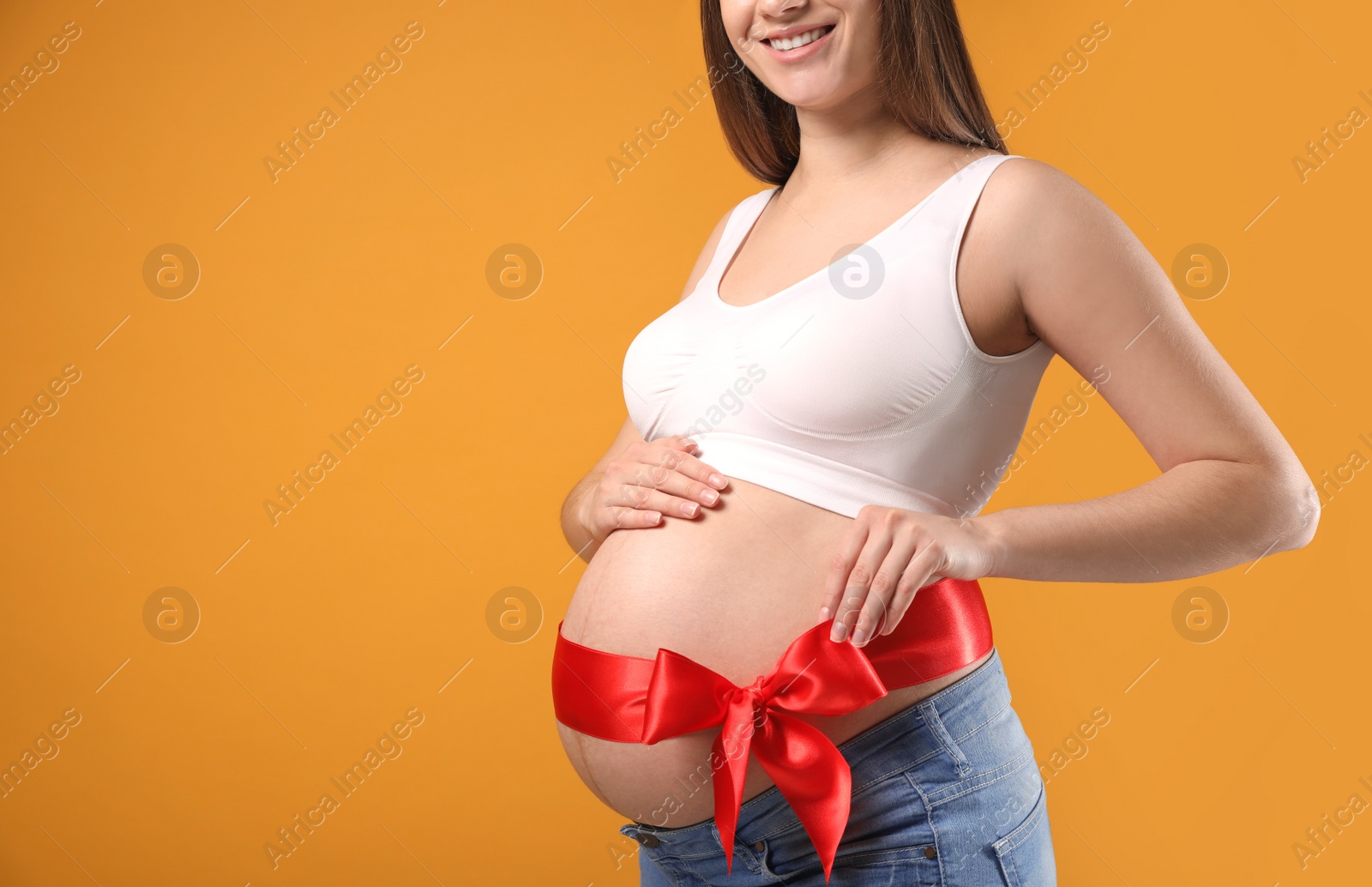 Young pregnant woman with red bow on her belly against yellow background, closeup and space for text. Time to give birth Photo of Young pregnant woman with red bow on her belly against yellow background, closeup and space for text. Time to give birth