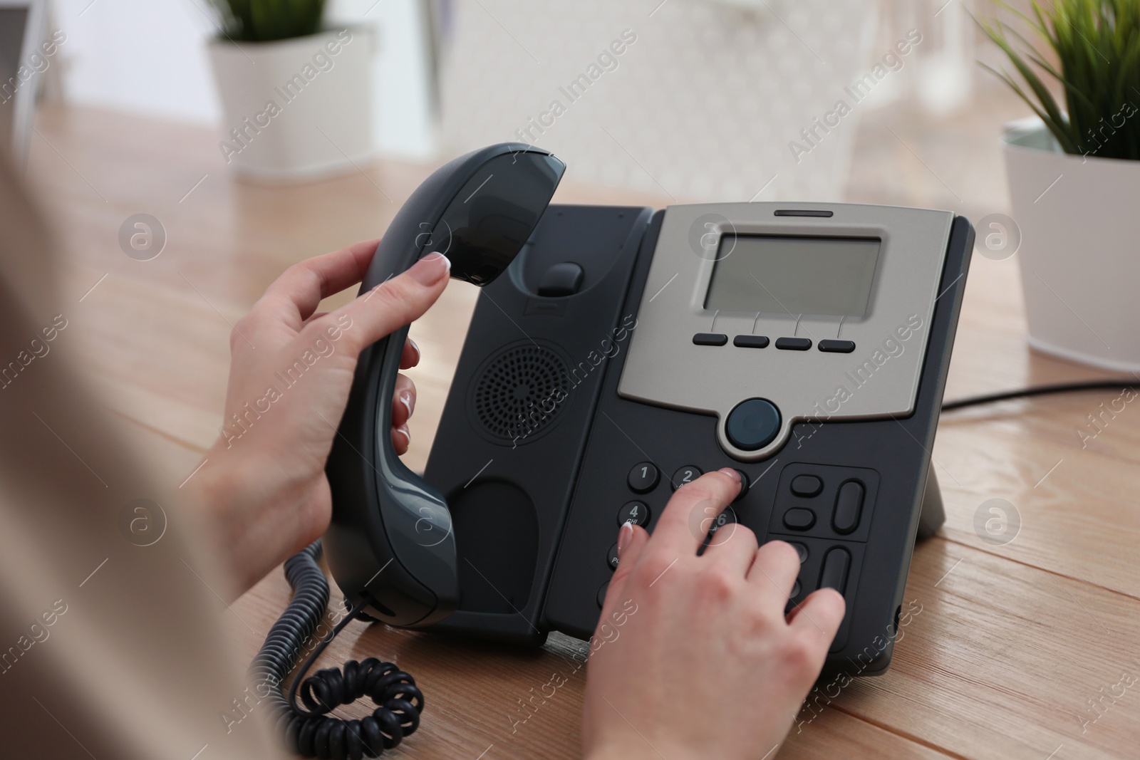Woman using desktop telephone at wooden table in office, closeup. Hotline service Photo of Woman using desktop telephone at wooden table in office, closeup. Hotline service