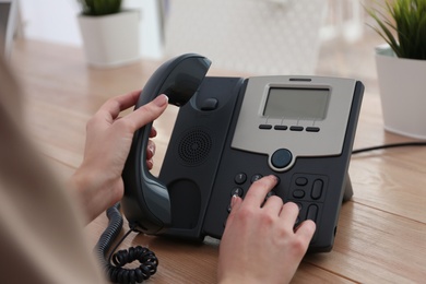 Woman using desktop telephone at wooden table in office, closeup. Hotline service Photo of Woman using desktop telephone at wooden table in office, closeup. Hotline service
