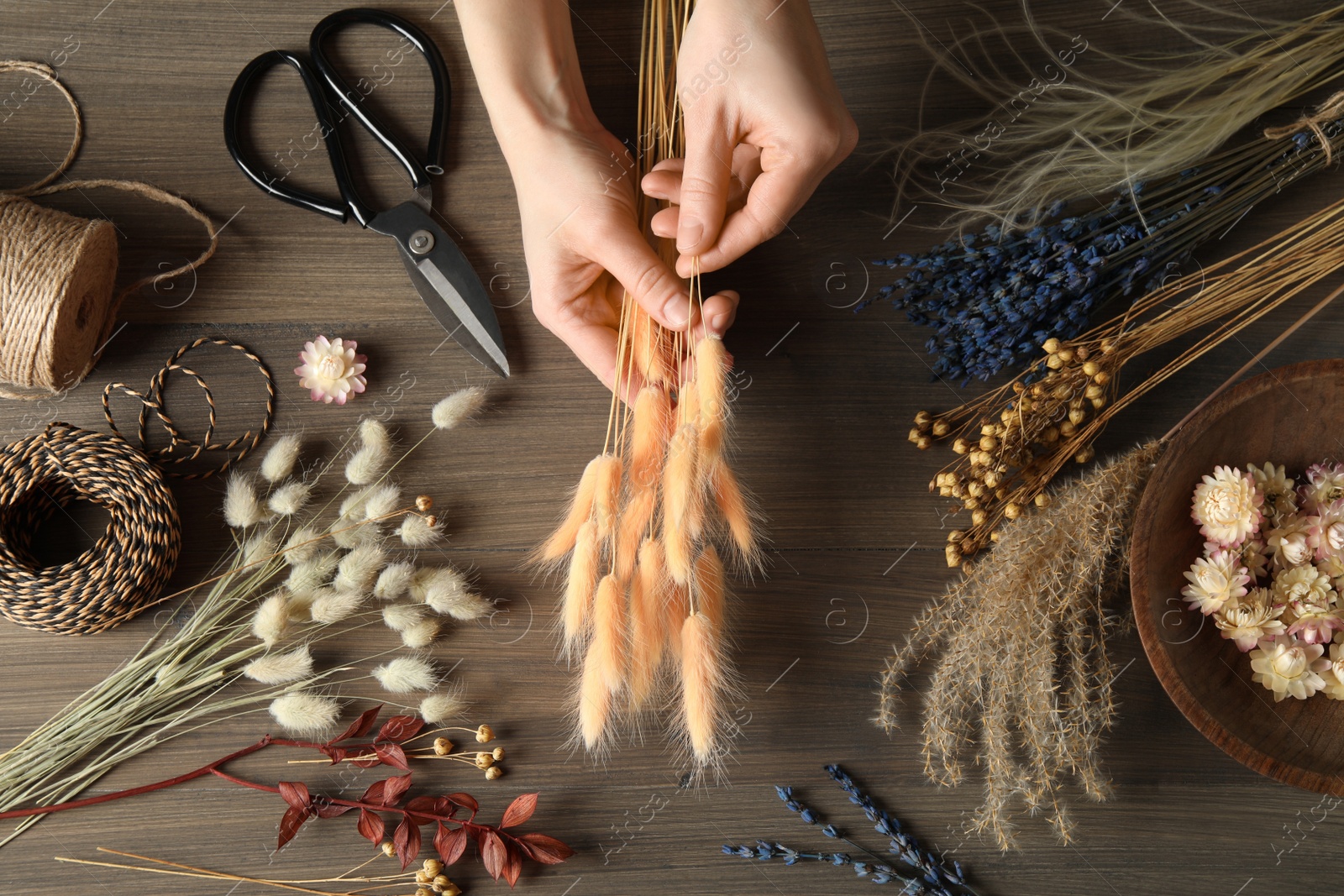 Florist making bouquet of dried flowers at wooden table, top view Photo of Florist making bouquet of dried flowers at wooden table, top view