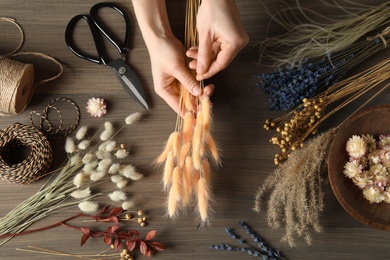 Florist making bouquet of dried flowers at wooden table, top view Photo of Florist making bouquet of dried flowers at wooden table, top view