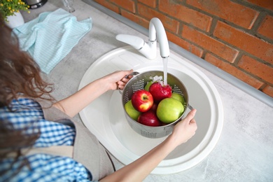 Young woman washing ripe apples in kitchen Photo of Young woman washing ripe apples in kitchen