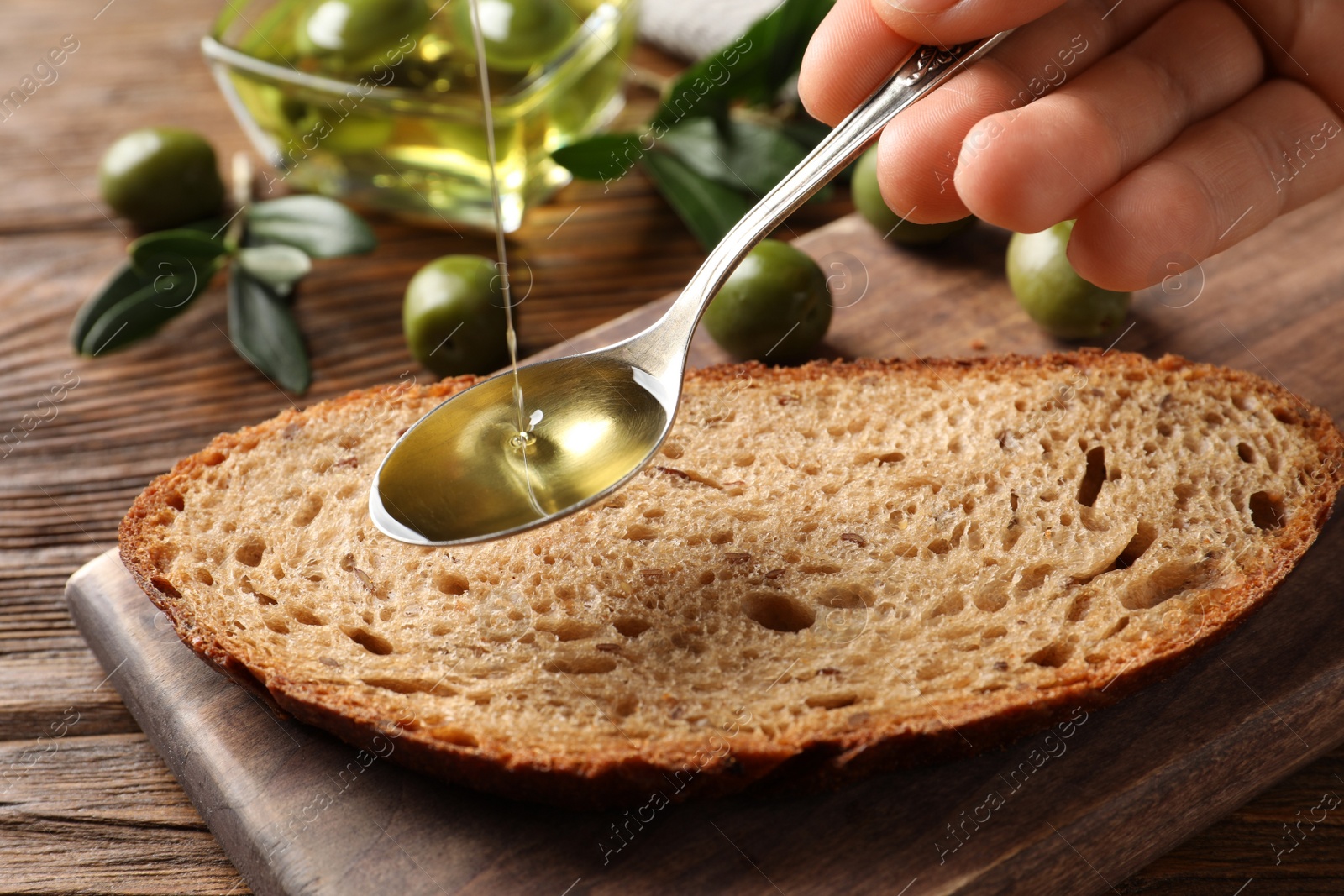 Woman pouring olive oil into spoon over bread at wooden table, closeup Photo of Woman pouring olive oil into spoon over bread at wooden table, closeup