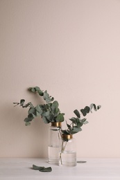 Vases with beautiful eucalyptus branches on white wooden table near beige wall. Space for text Photo of Vases with beautiful eucalyptus branches on white wooden table near beige wall. Space for text