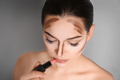 Young woman applying lipstick on grey background. Professional makeup products Photo of Young woman applying lipstick on grey background. Professional makeup products