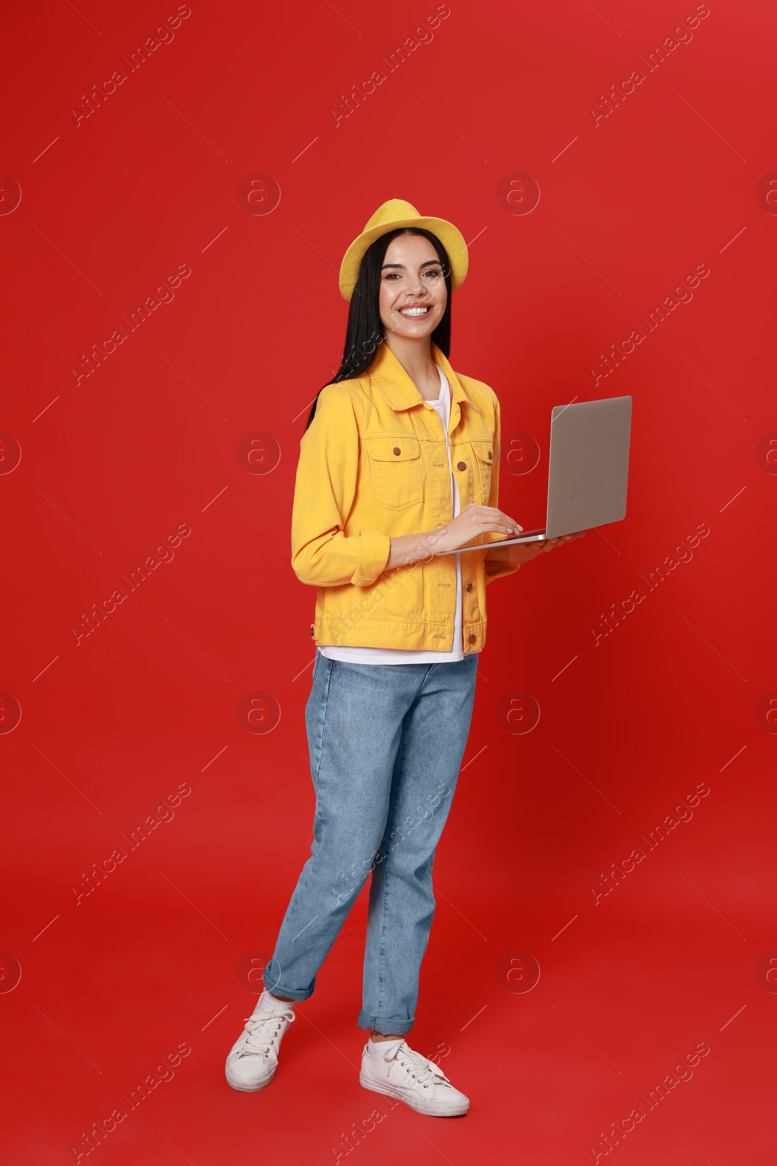 Young woman with modern laptop walking on red background Photo of Young woman with modern laptop walking on red background
