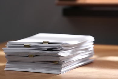 Stack of blank paper with binder clips on wooden table indoors Photo of Stack of blank paper with binder clips on wooden table indoors