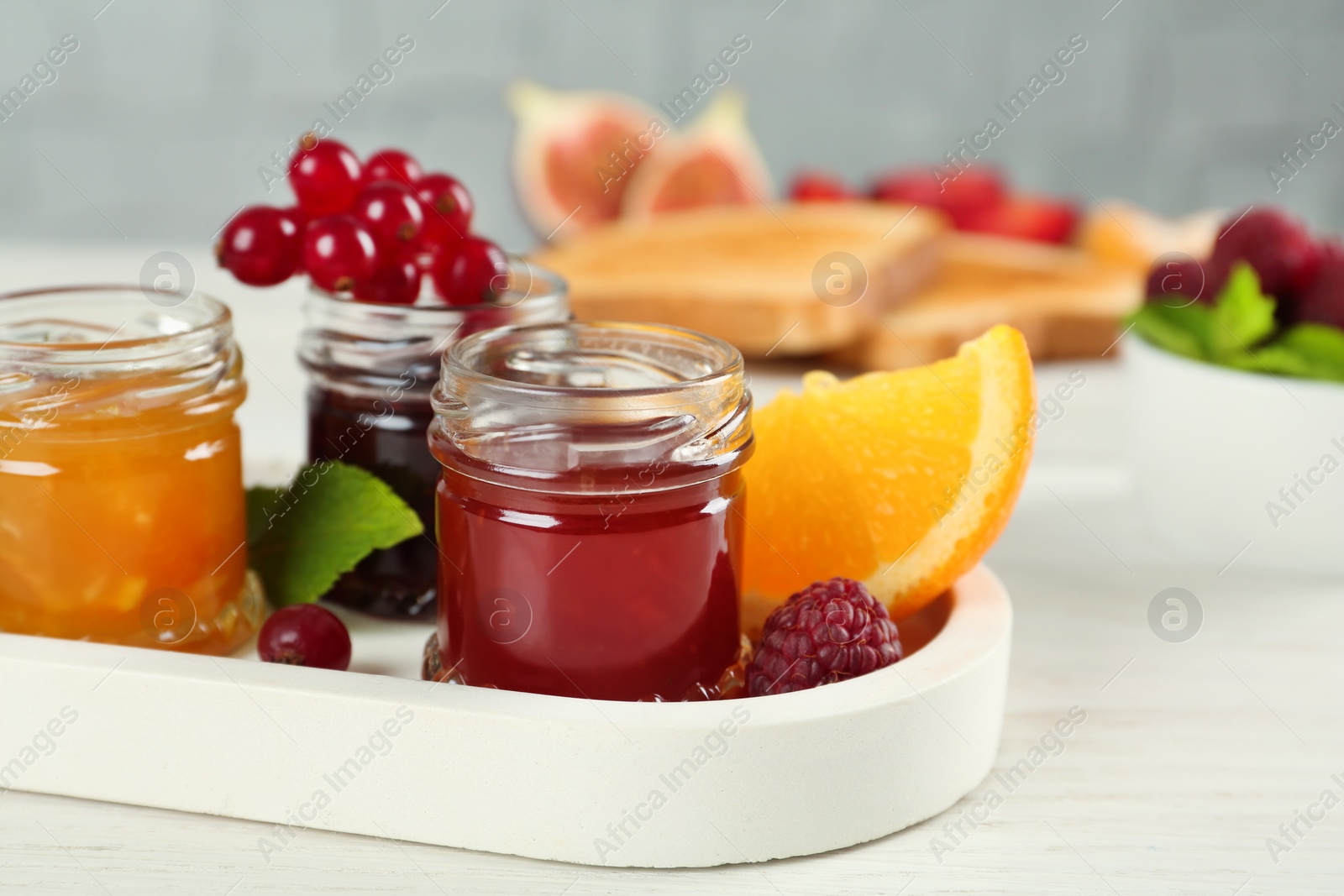Jars with different sweet jams and ingredients on white wooden table Photo of Jars with different sweet jams and ingredients on white wooden table