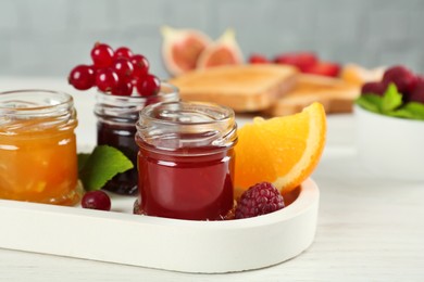 Jars with different sweet jams and ingredients on white wooden table Photo of Jars with different sweet jams and ingredients on white wooden table