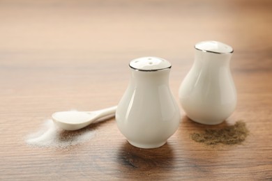White ceramic salt and pepper shakers with spoon on wooden table, closeup Photo of White ceramic salt and pepper shakers with spoon on wooden table, closeup