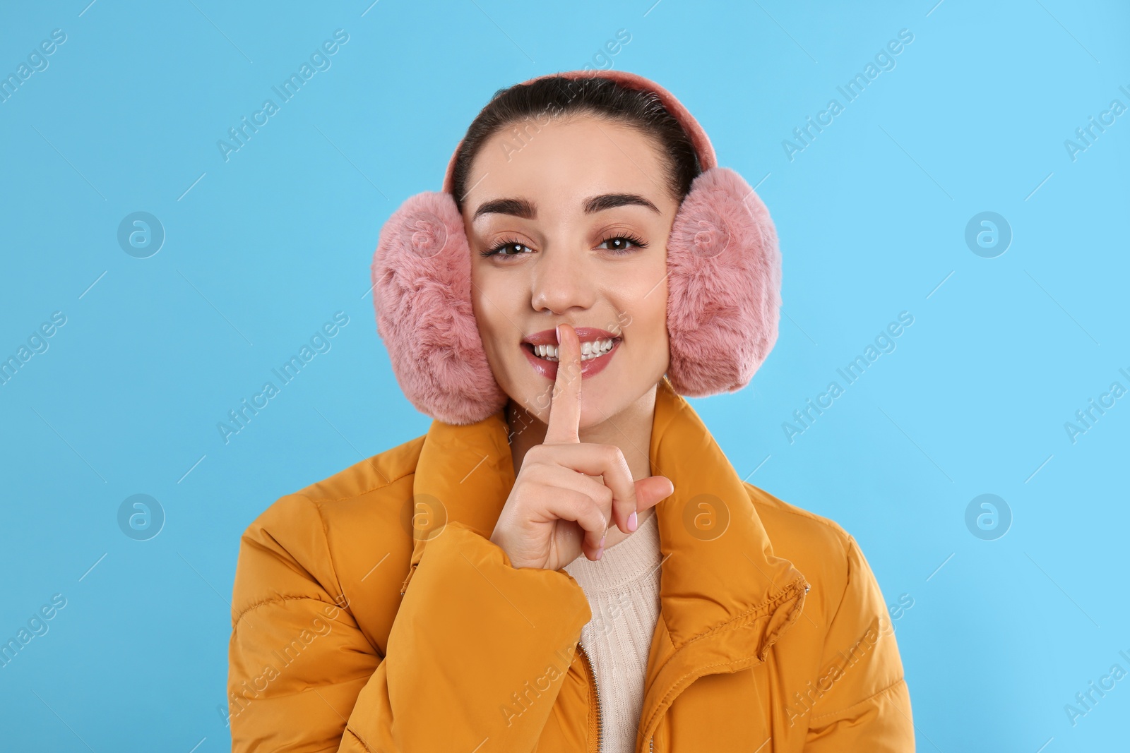 Beautiful young woman wearing earmuffs on light blue background Photo of Beautiful young woman wearing earmuffs on light blue background