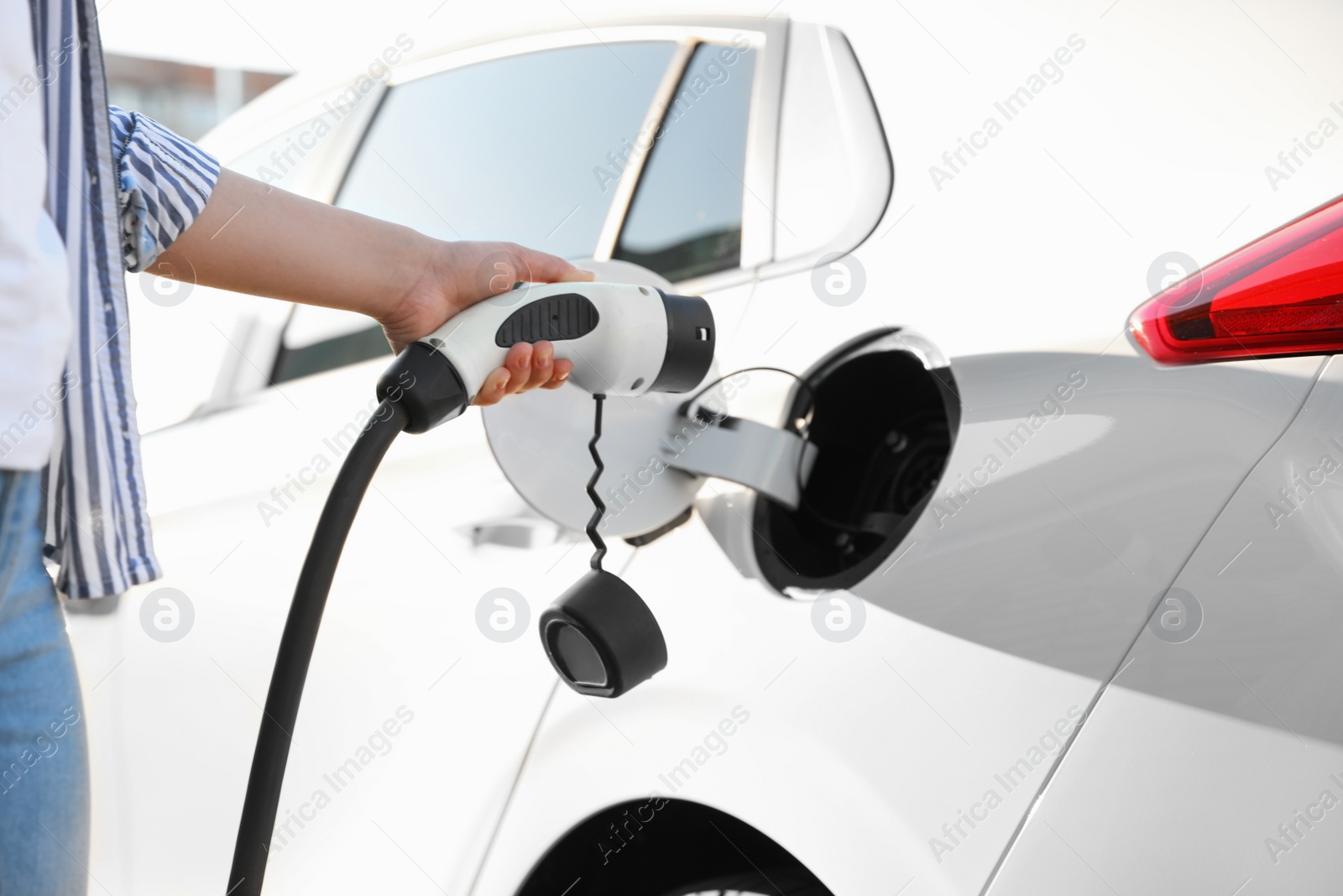 Woman inserting plug into electric car socket at charging station, closeup Photo of Woman inserting plug into electric car socket at charging station, closeup