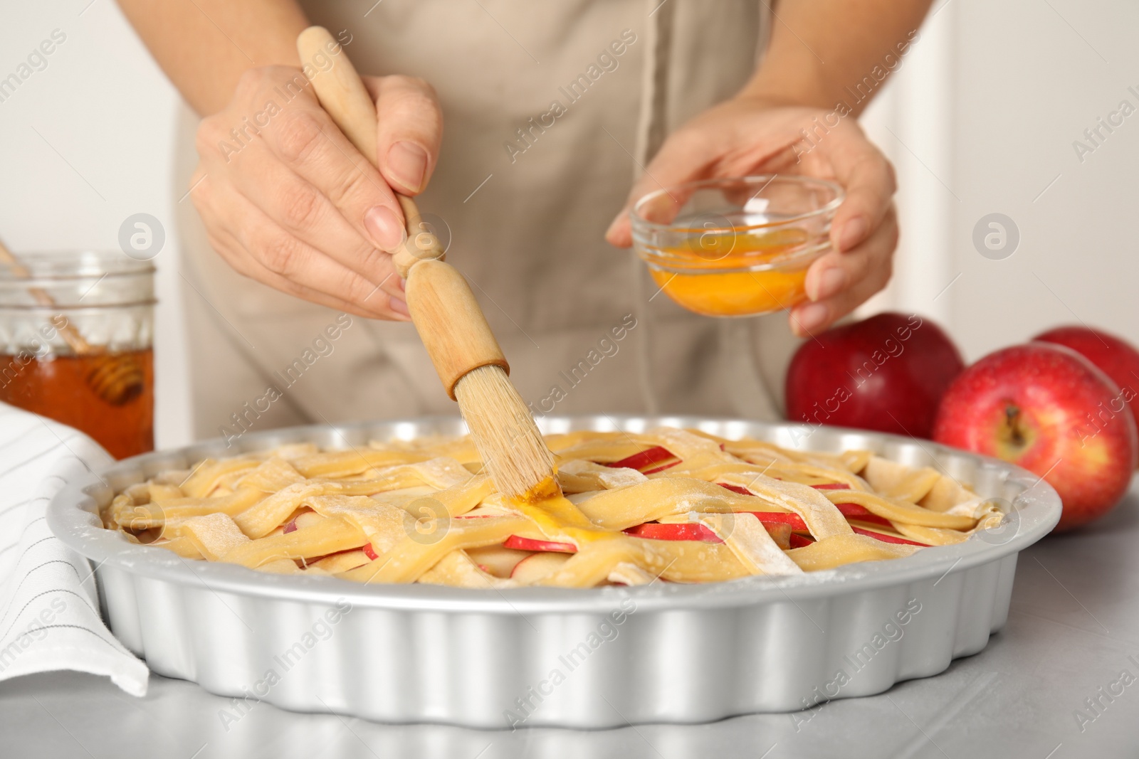Woman applying liquid egg onto traditional English apple pie with brush at light grey table, closeup Photo of Woman applying liquid egg onto traditional English apple pie with brush at light grey table, closeup