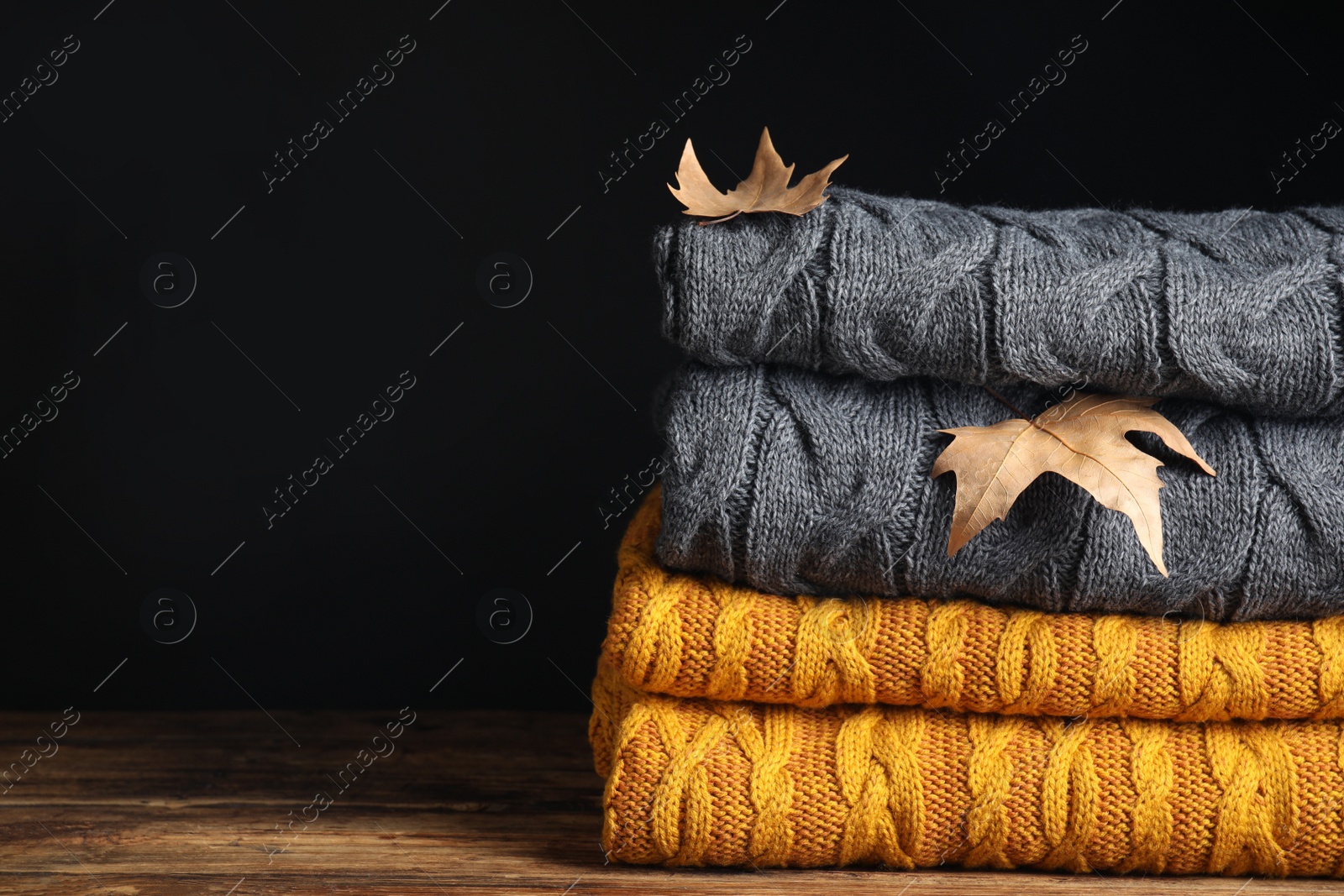 Grey and orange knitted plaids with dry leaves on wooden table, closeup. Space for text Photo of Grey and orange knitted plaids with dry leaves on wooden table, closeup. Space for text