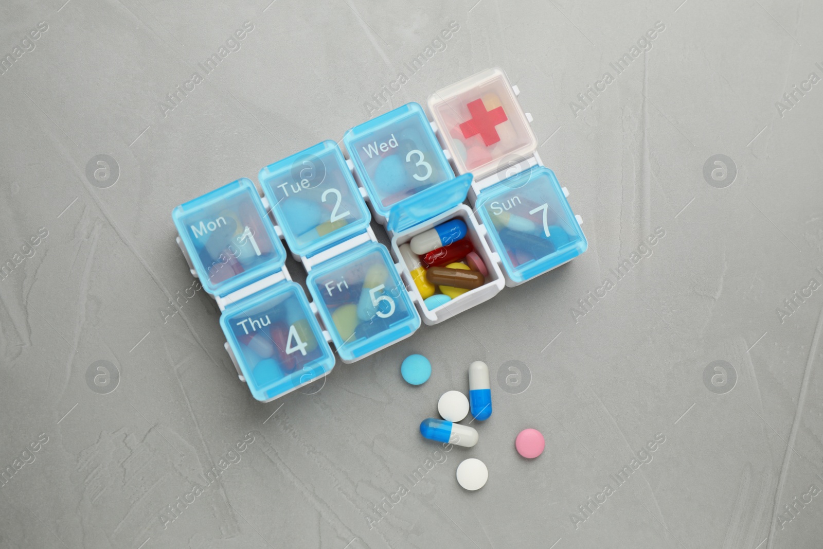 Plastic box with different pills on light grey stone table, flat lay Photo of Plastic box with different pills on light grey stone table, flat lay