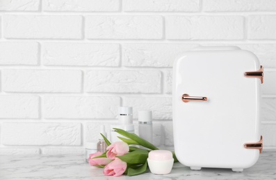 Cosmetic refrigerator and skin care products on white marble table, space for text Photo of Cosmetic refrigerator and skin care products on white marble table, space for text