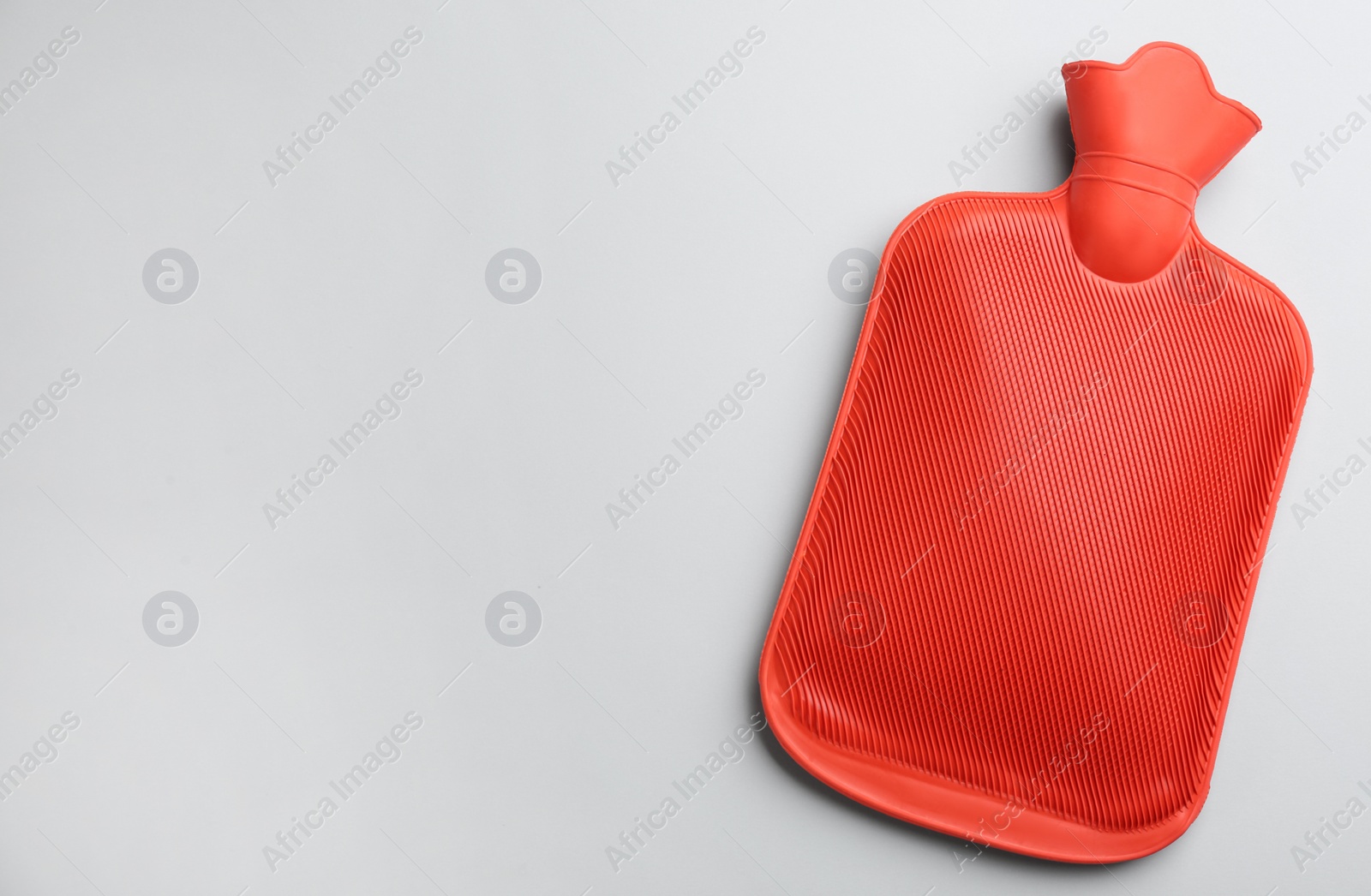 Photo of Red rubber hot water bottle on light background, top view. Space for text