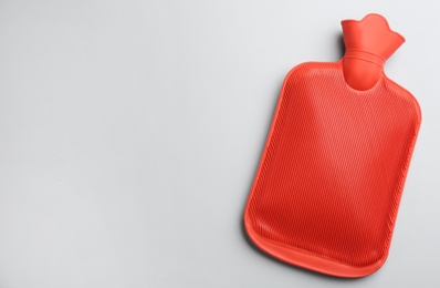 Photo of Red rubber hot water bottle on light background, top view. Space for text