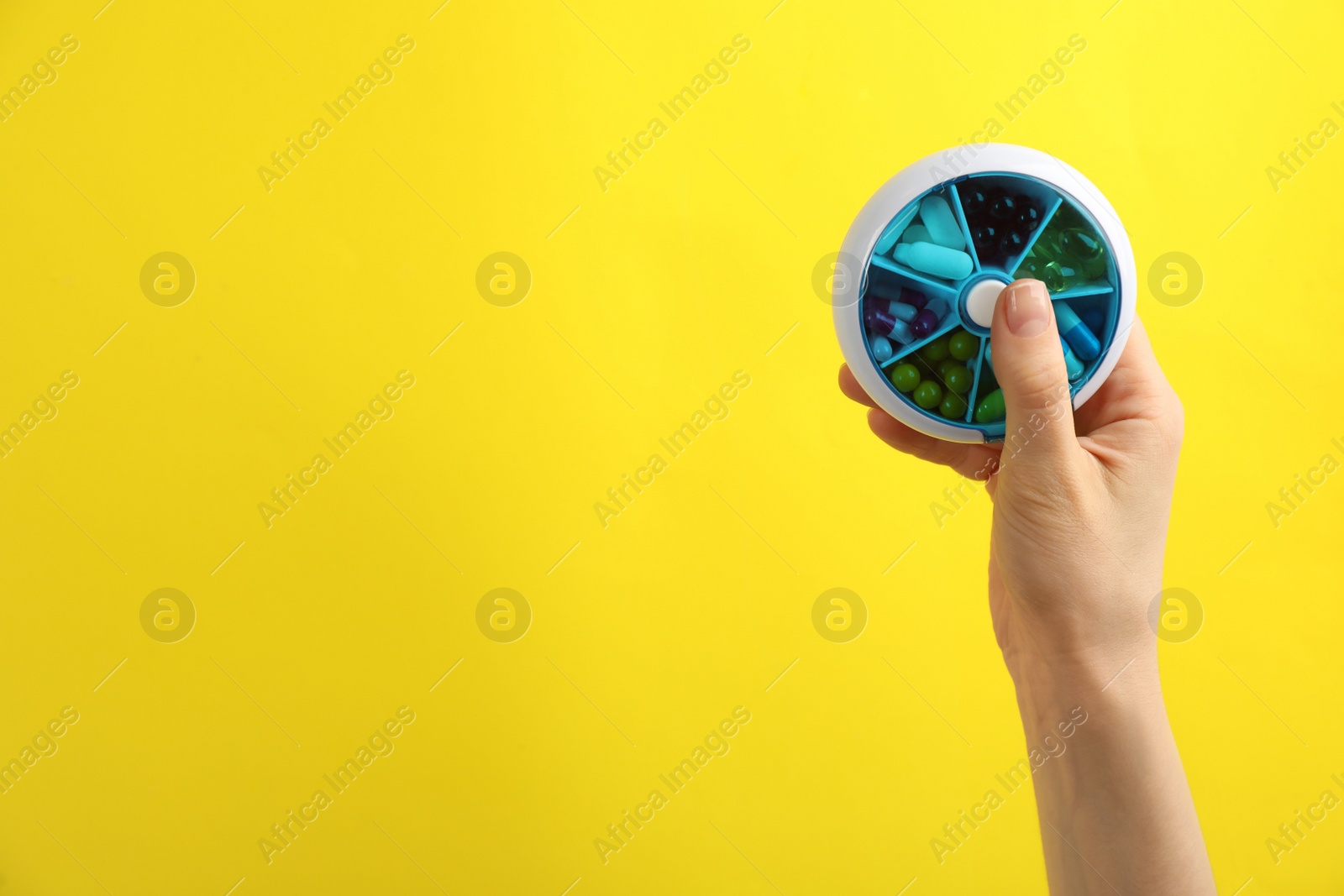 Woman holding plastic box with different pills on yellow background, closeup. Space for text Photo of Woman holding plastic box with different pills on yellow background, closeup. Space for text