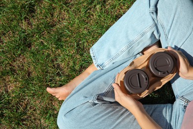 Woman holding takeaway cardboard coffee cups with plastic lids on green grass, top view. Space for text Photo of Woman holding takeaway cardboard coffee cups with plastic lids on green grass, top view. Space for text
