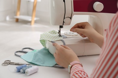 Woman making cloth mask with sewing machine at white table, closeup Photo of Woman making cloth mask with sewing machine at white table, closeup