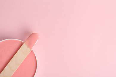 Wooden spatula and hot depilatory wax on light pink background, top view. Space for text Photo of Wooden spatula and hot depilatory wax on light pink background, top view. Space for text