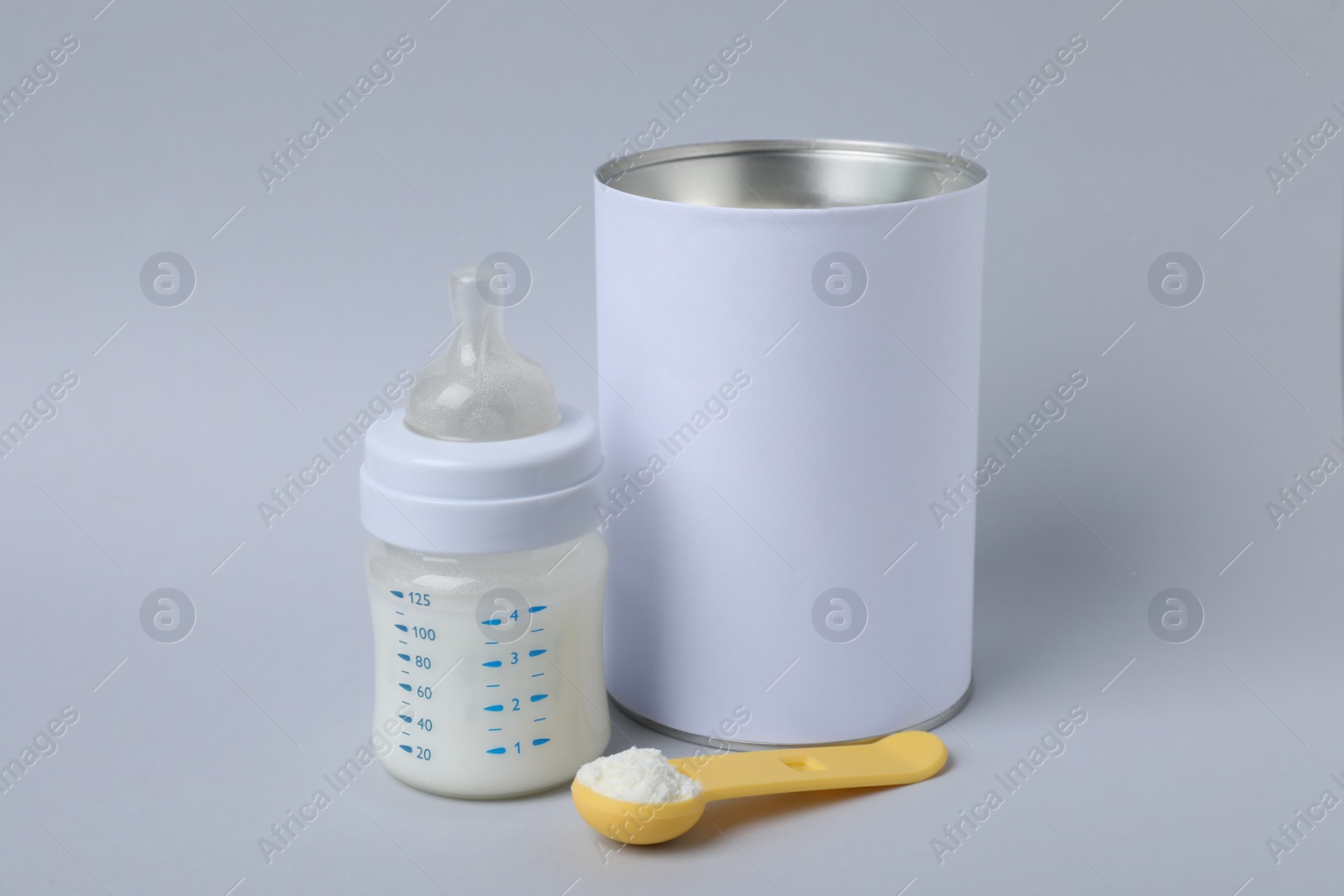 Blank can of powdered infant formula with scoop and feeding bottle on light grey background. Baby milk Photo of Blank can of powdered infant formula with scoop and feeding bottle on light grey background. Baby milk