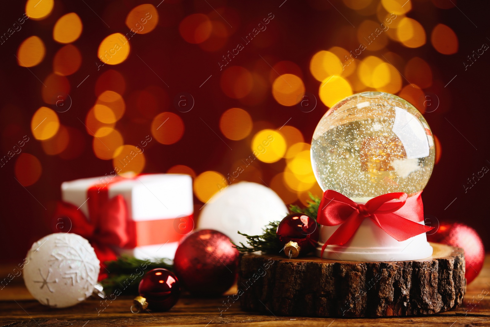 Beautiful snow globe and Christmas decor on wooden table against blurred festive lights Photo of Beautiful snow globe and Christmas decor on wooden table against blurred festive lights