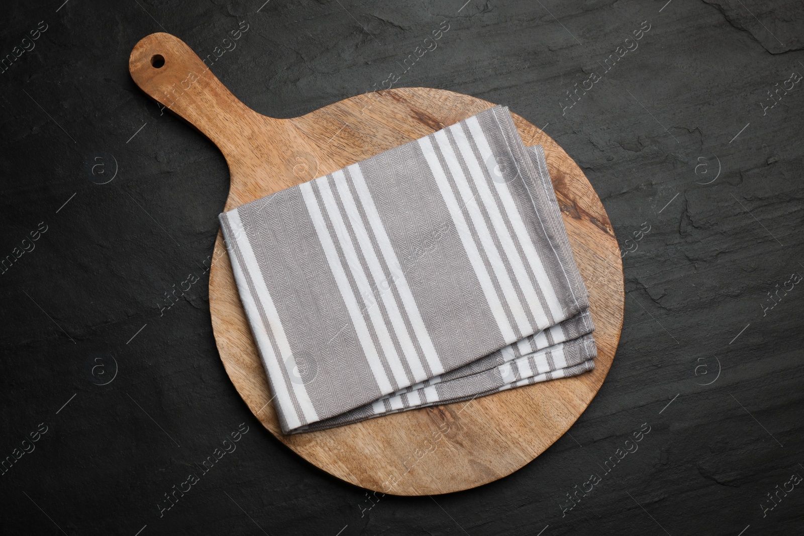 Striped kitchen towel and wooden cutting board on black table, top view Photo of Striped kitchen towel and wooden cutting board on black table, top view