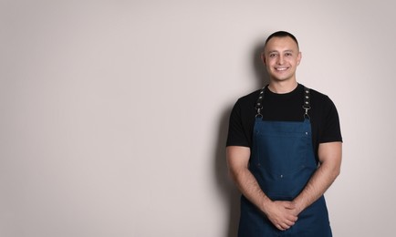 Portrait of happy young waiter in uniform on light background Photo of Portrait of happy young waiter in uniform on light background