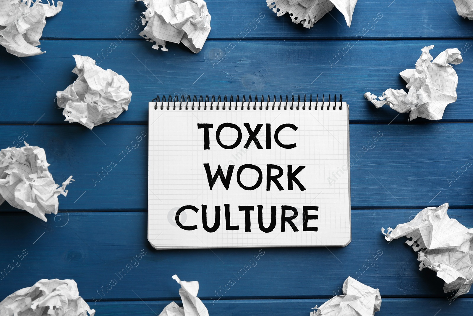 Notebook with text Toxic Work Culture and crumpled paper on blue wooden table, flat lay Image of Notebook with text Toxic Work Culture and crumpled paper on blue wooden table, flat lay