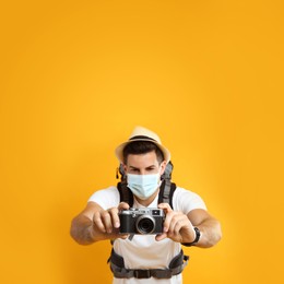 Male tourist in protective mask with travel backpack taking picture against yellow background, focus on camera Photo of Male tourist in protective mask with travel backpack taking picture against yellow background, focus on camera
