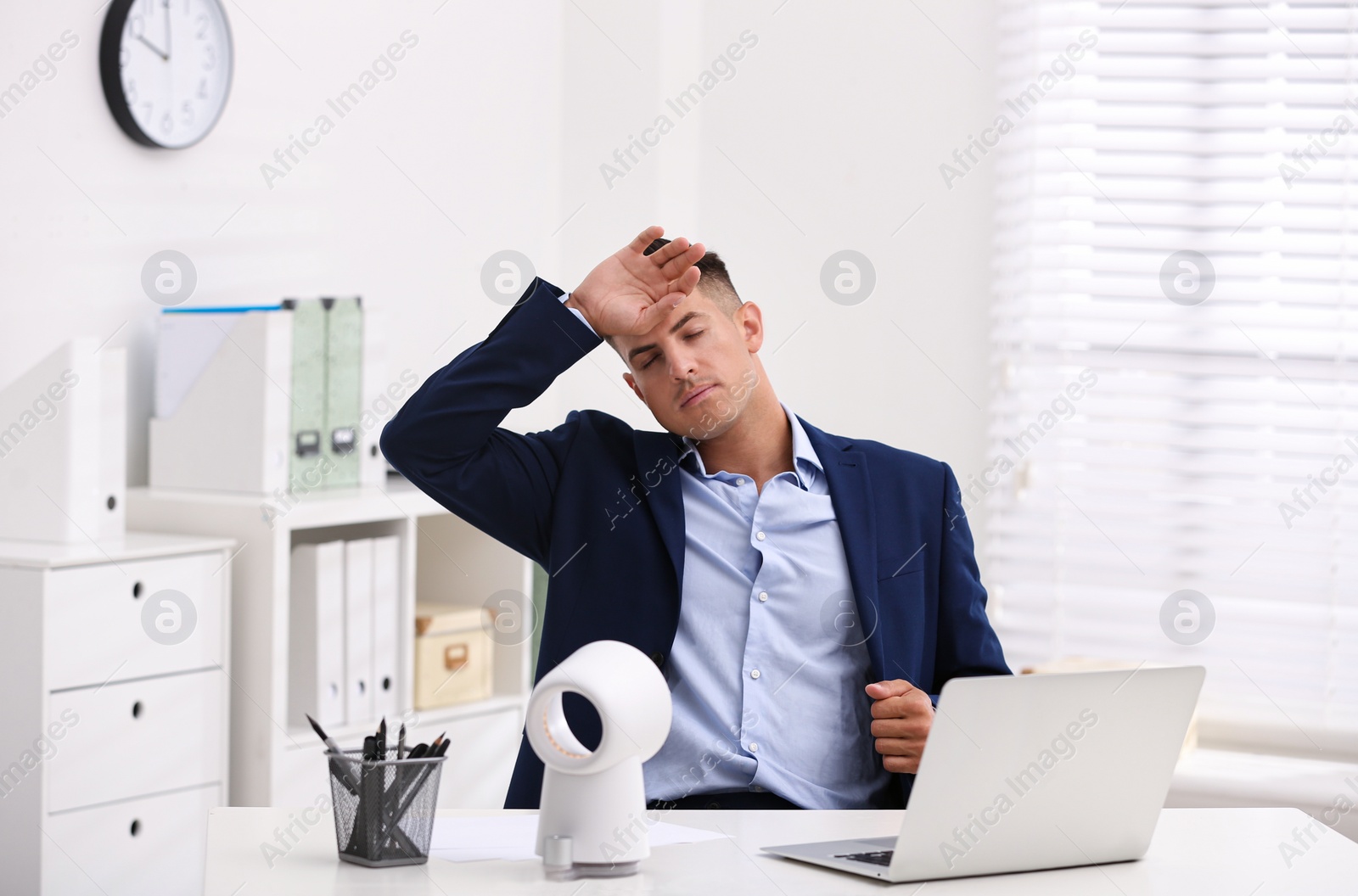 Man suffering from heat in front of fan at workplace Photo of Man suffering from heat in front of fan at workplace
