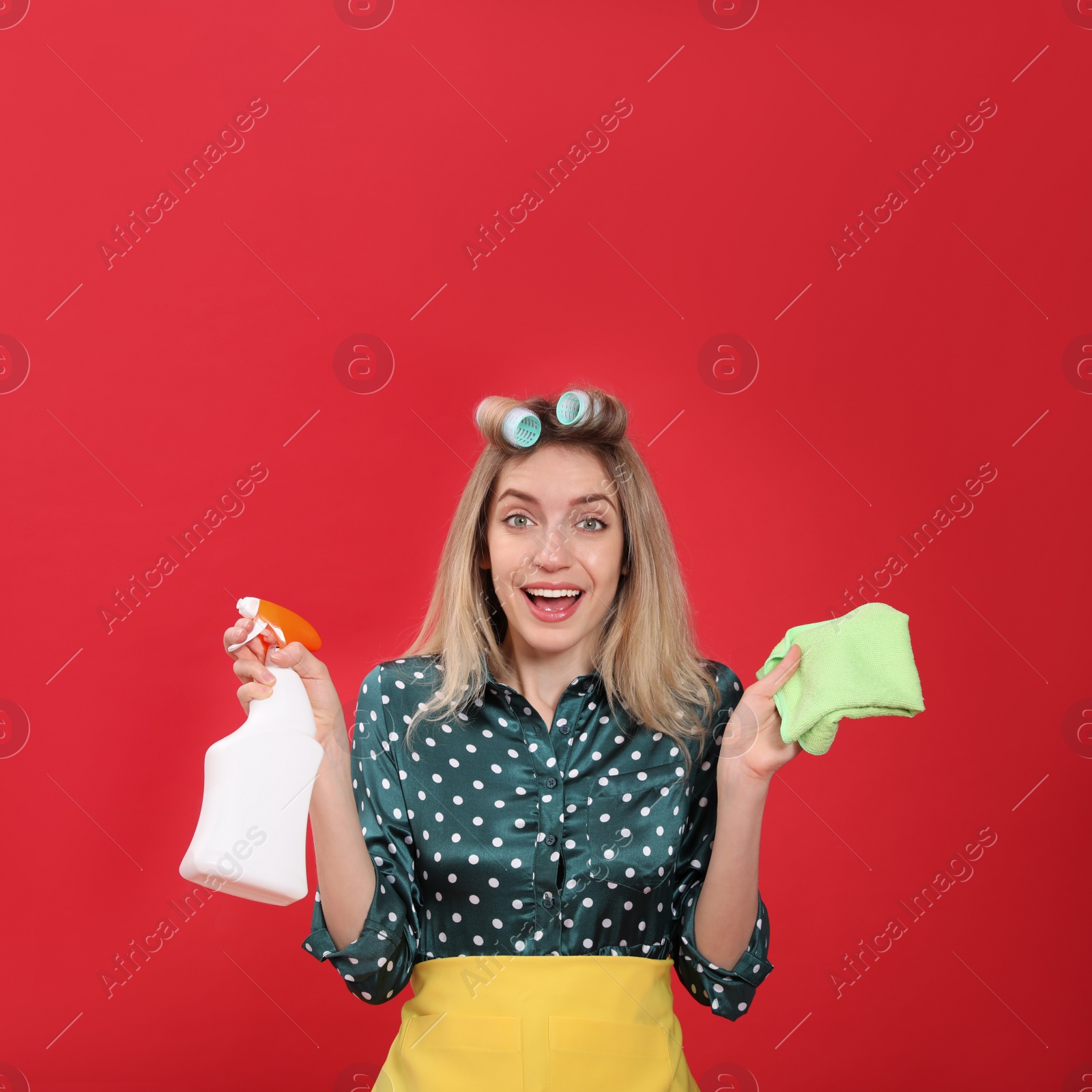 Young housewife with detergent and rag on red background Photo of Young housewife with detergent and rag on red background