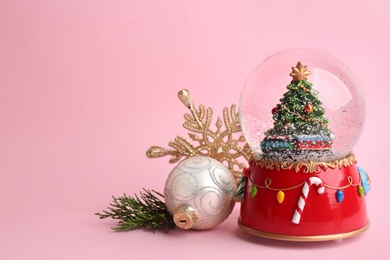 Beautiful snow globe and Christmas decor on pink background, space for text Photo of Beautiful snow globe and Christmas decor on pink background, space for text