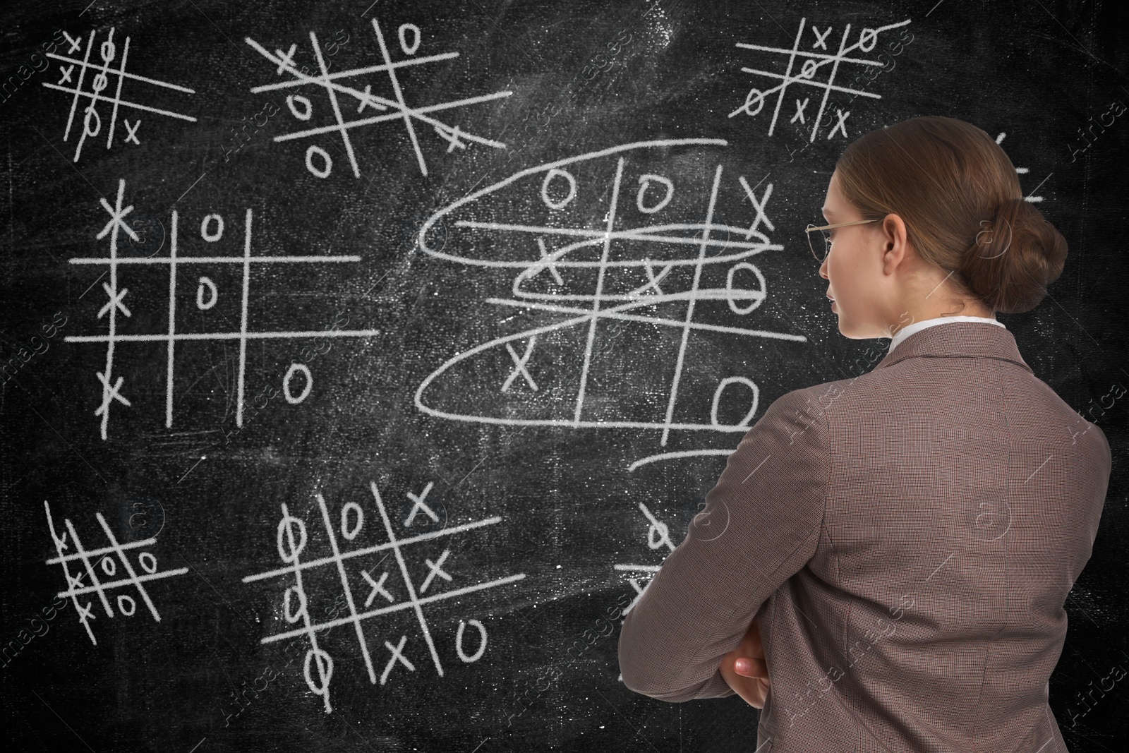 Young businesswoman in elegant suit near blackboard with drawn tic tac toe game Image of Young businesswoman in elegant suit near blackboard with drawn tic tac toe game
