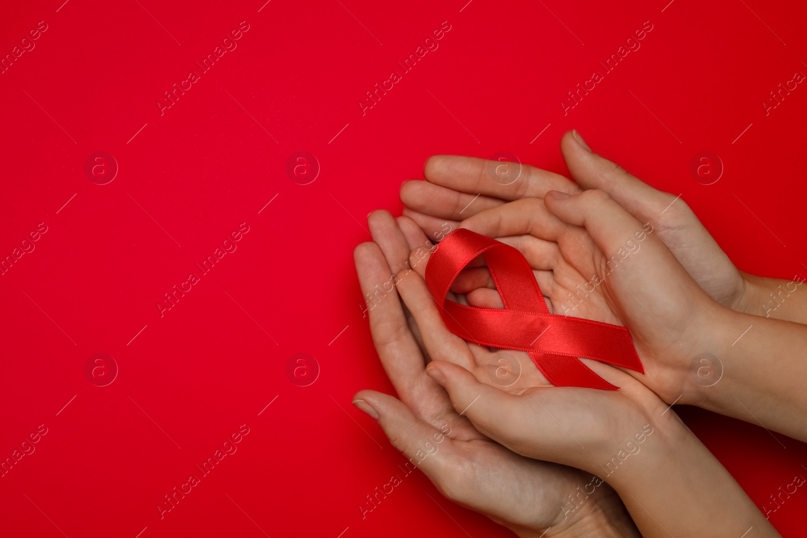 Woman and girl holding red ribbon on bright background, top view with space for text. AIDS disease awareness Photo of Woman and girl holding red ribbon on bright background, top view with space for text. AIDS disease awareness