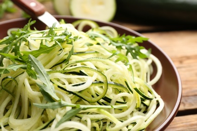 Tasty zucchini pasta with arugula on wooden table, closeup Photo of Tasty zucchini pasta with arugula on wooden table, closeup
