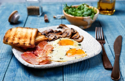 Plate with fried eggs, bacon, mushrooms and toasts on wooden background Photo of Plate with fried eggs, bacon, mushrooms and toasts on wooden background