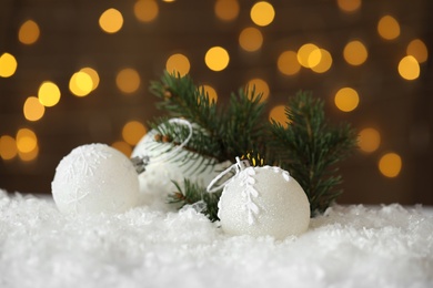 Beautiful Christmas balls and fir branch on snow against blurred festive lights Photo of Beautiful Christmas balls and fir branch on snow against blurred festive lights