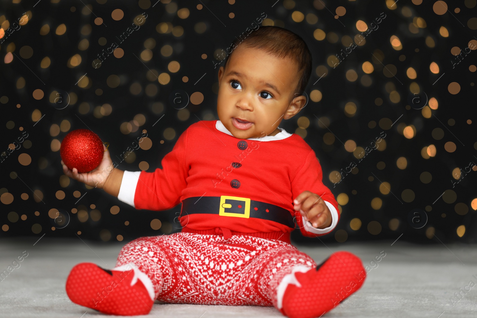 Cute little African American baby with Christmas ball and blurred lights on dark background Image of Cute little African American baby with Christmas ball and blurred lights on dark background