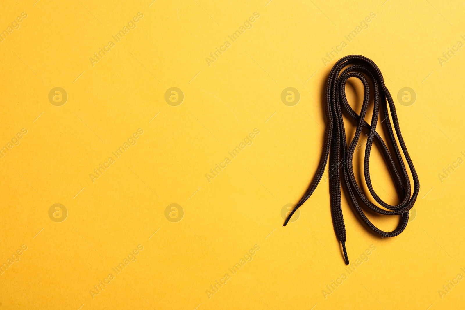 Brown shoelace on yellow background, top view. Space for text Photo of Brown shoelace on yellow background, top view. Space for text