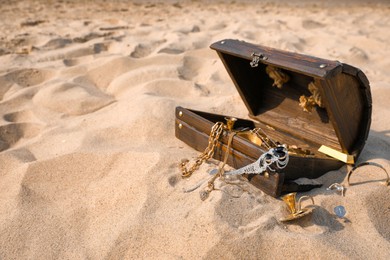 Open wooden chest with treasures on sand, space for text Photo of Open wooden chest with treasures on sand, space for text